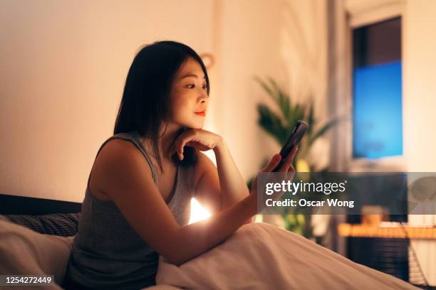 young woman using smart phone before bedtime - smartphone lesen nacht stock-fotos und bilder