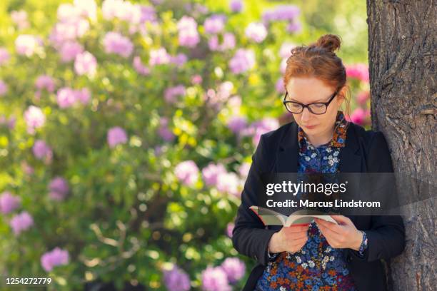 una mujer leyendo un libro en un jardín - libro en rústica fotografías e imágenes de stock