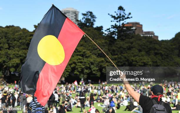 Man holds the Aboriginal flag as people gather at a rally against Black Deaths in Custody in The Domain on July 05, 2020 in Sydney, Australia. The...