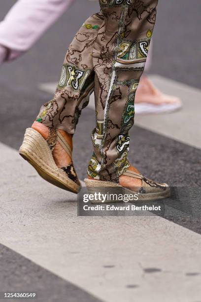 Passerby wears silky flowing pants with printed patterns, wedge shoes with straw soles and snake print, on July 04, 2020 in Paris, France.