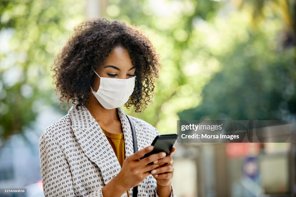 Businesswoman using smart phone during COVID-19 pandemic in city, She is Wearing Protective Face Mask