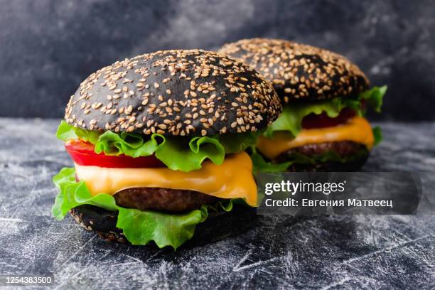 two black bun burgers with beef meat cutlet, cheese, vegetables on dark background - close up bread roll black backdrop horizontal stock pictures, royalty-free photos & images