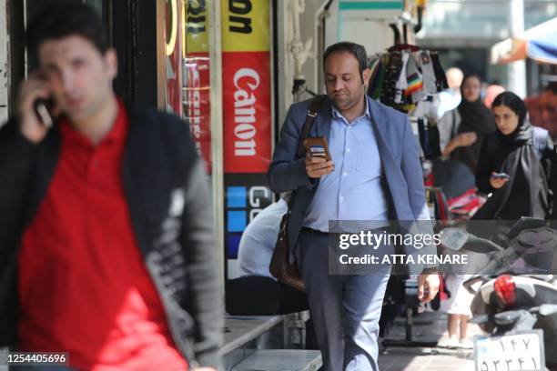 In this picture taken on April 19 people use their mobile telephones as they walk along a street in Tehran. The popularity of Iran's domestic...