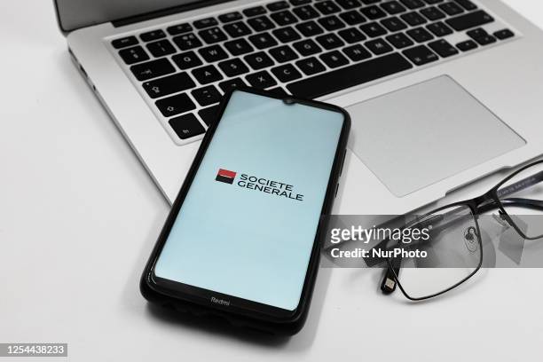 In this photo illustration a Societe Generale bank logo is displayed on a smartphone screen above a notebook next to glasses and a Macbook in Athens,...