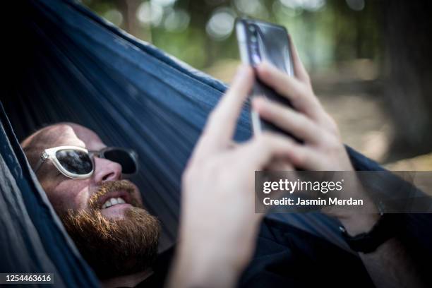 relaxed man sitting in hammock using smartphone - hammock phone stock pictures, royalty-free photos & images