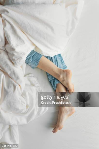 pies de mujer en pijama azul durmiendo en la cama - woman cross legs fotografías e imágenes de stock