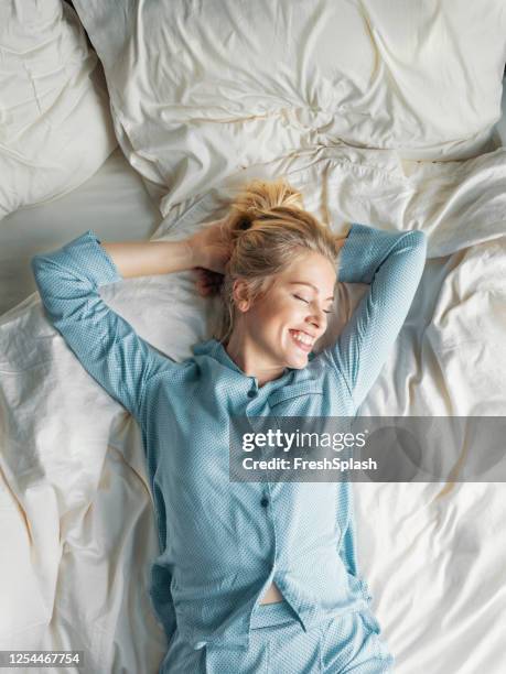 weekend ochtenden: een mooie blonde vrouw in blauwe pyjama's liggend in bed in de ochtend - pyjama stockfoto's en -beelden