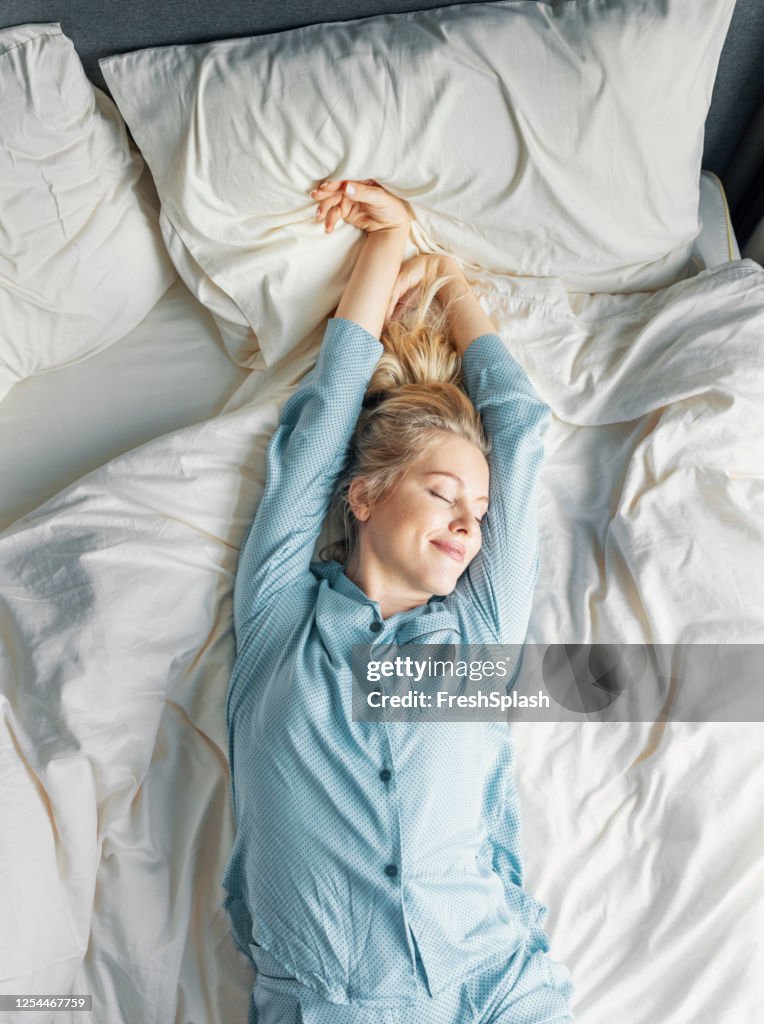 Wochenendmorgen: eine schöne blonde Frau in blauen Pyjamas, die morgens im Bett liegt