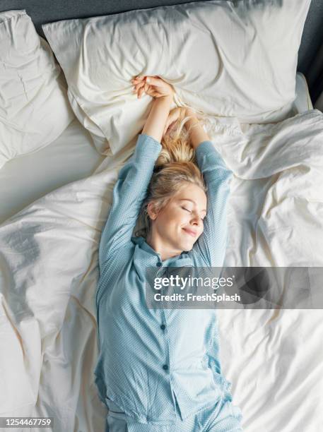 weekend ochtenden: een mooie blonde vrouw in blauwe pyjama's liggend in bed in de ochtend - beautiful women bed stockfoto's en -beelden