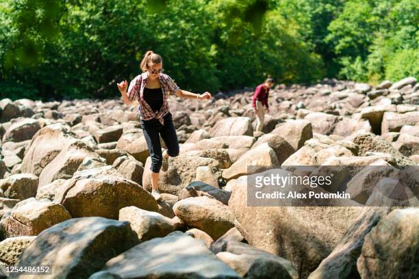 teenage girls explore walking across a boulderfield in poconos, pennsylvania, usa, on a summer sunny day. - pocono stock pictures, royalty-free photos & images
