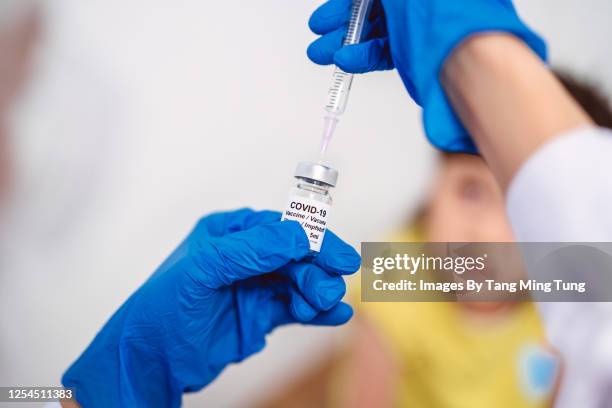 medical doctor in protective gloves filling injection syringe with covid-19 vaccine and ready to give kid girl covid-19 vaccination - covid 19 vaccine stock-fotos und bilder