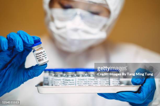 healthcare professional in protective gloves & workwear holding & organising a tray of covid-19 vaccine vials - china virus stock-fotos und bilder