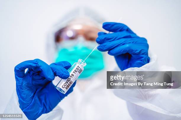 doctor in protective gloves & workwear holding open test tube and taking out sampling swab for novel covid-19 test - coronavirus test stockfoto's en -beelden