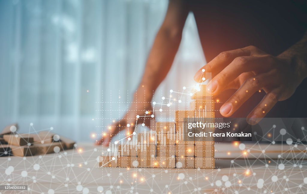 Hand of a businesswoman is arranging wooden toys as steps along the rising graph.Concept for business growth success process