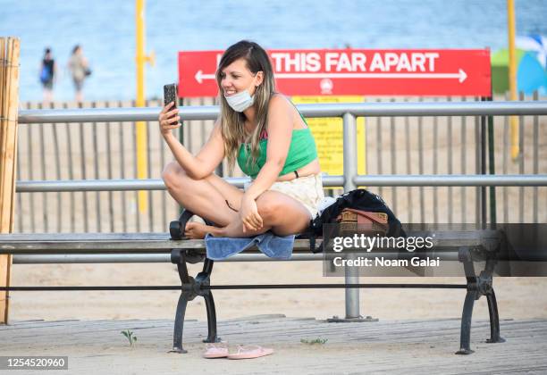 Person wears a face mask on her chin while speaking on the phone at Brighton Beach in Coney Island as New York City moves into Phase 2 of re-opening...