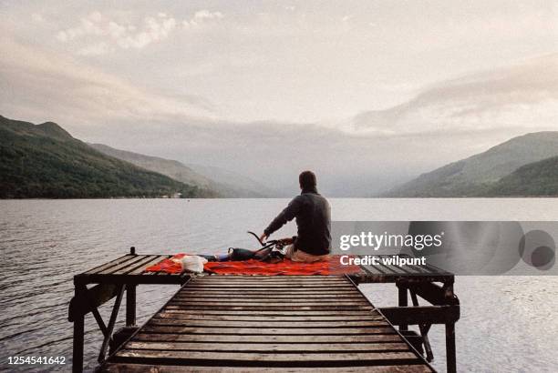 mann sitzt auf einer masai decke auf einem hölmann an einem schottischen highlands loch - highlands schottland wandern stock-fotos und bilder