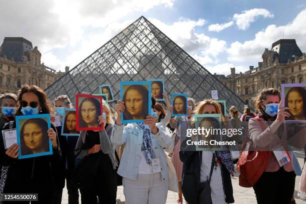 Paris tour guides wearing protective face masks hold posters depicting the Mona Lisa painting by Italian artist Leonardo da Vinci at Le Louvre museum...