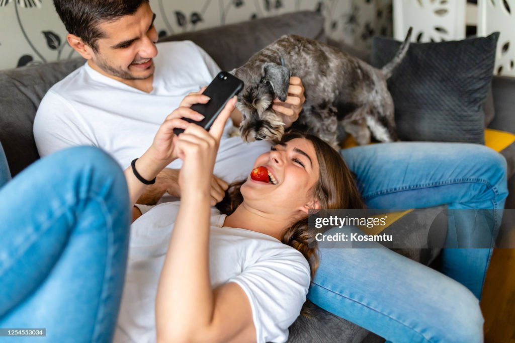 Gelukkige vrouw die selfie neemt terwijl haar hond aardbei in haar mond probeert te stelen