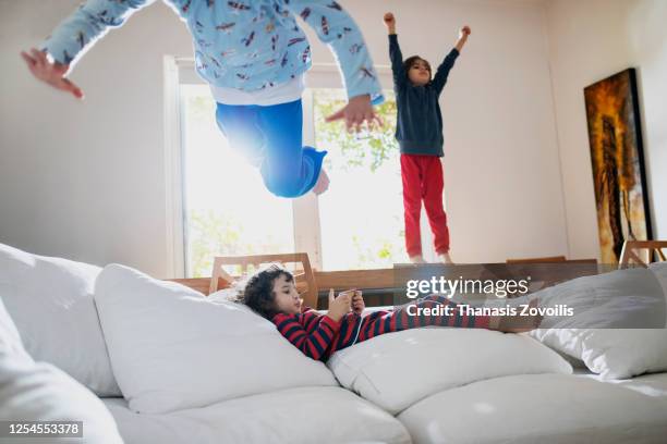 small kids having fun indoor while their brother using a digital tablet - gruppe springen ipad stock-fotos und bilder