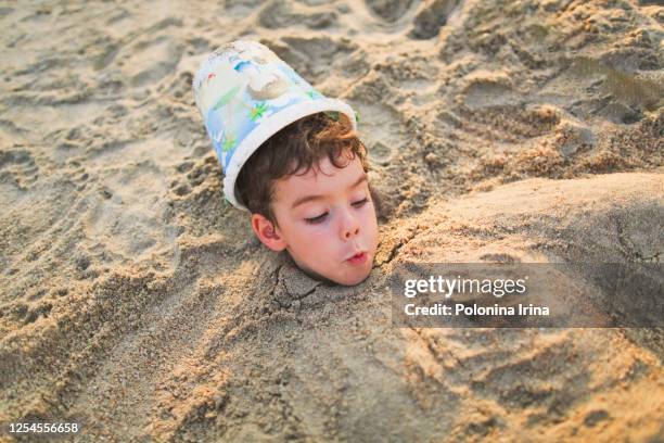 little funny boy playing on the sea beach. - head in sand stock-fotos und bilder