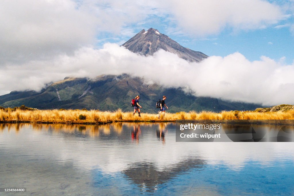 Hikers Reflection of Mount Taranaki Egmont in natural lake middle