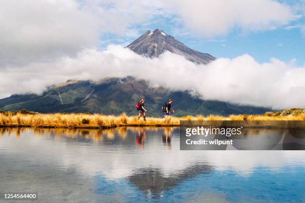 hikers reflection of mount taranaki egmont in natural lake middle - new zealand stock pictures, royalty-free photos & images
