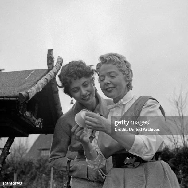 Die deutschen Schlagersängerinnen Margot Eskens und Friedel Hensch im Garten an einem Vogelhäuschen, Deutschland 1956.
