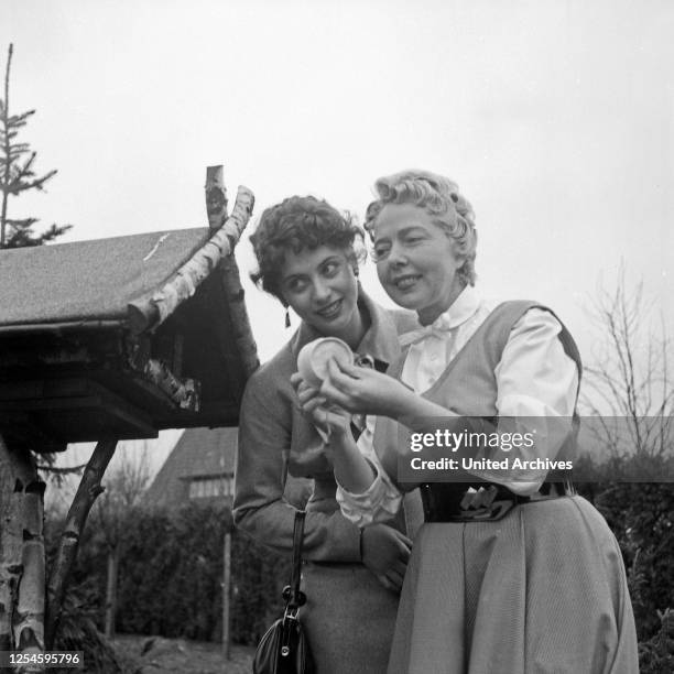 Die deutschen Schlagersängerinnen Margot Eskens und Friedel Hensch im Garten an einem Vogelhäuschen, Deutschland 1956.