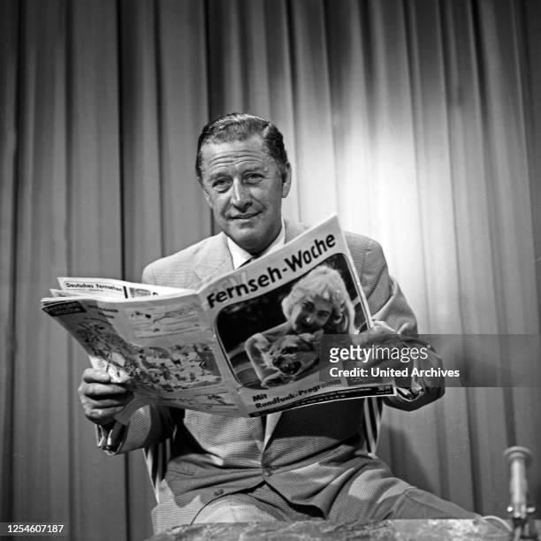 Der deutsche Schauspieler Hans Söhnker wirft einen Blick in die Zeitschrift "TV Fernsehwoche", Deutschland 1950er Jahre.