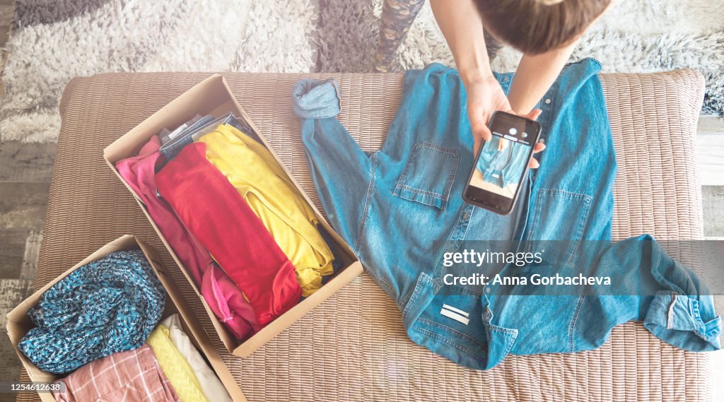 Woman taking photo of denim shirt on smartphone to sell it on internet shop.