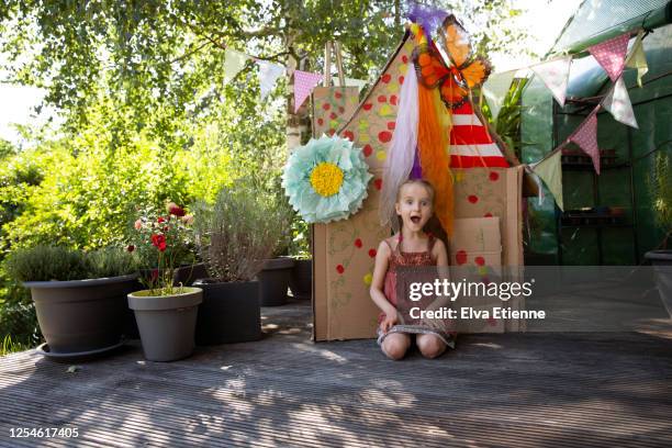 happy child (6-7) sitting next to a homemade playhouse made from recycled cardboard and decorated with multi-coloured paints and materials - playhouse stockfoto's en -beelden