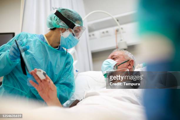 one nurse showing a framed photograph of a relative to a covid patient. - intensive care unit stock pictures, royalty-free photos & images