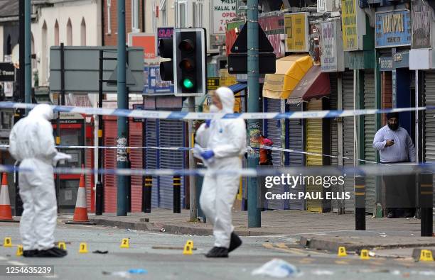 Man checks his mobile phone as police forensics officers examine the scene in Birmingham, central England, on August 10, 2011 where three Asian men...