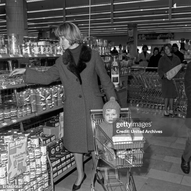 Eine Kundin mit ihrem Kind im Einkaufswagen auf ihrem Gang durch einen Supermarkt in Hamburg, Deutschland, Anfang 1960er Jahre.