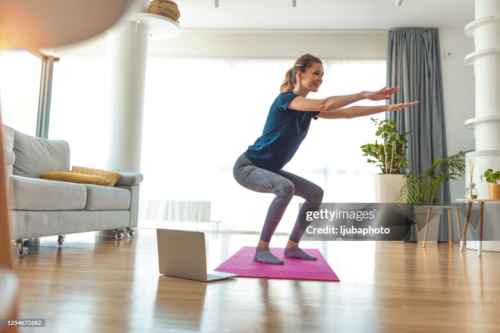 Full length of beautiful young woman in sports clothing crouching while exercising at home