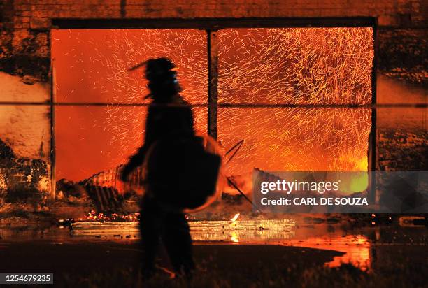 British riot policemen walks past a burning 140 year old furniture store in Croydon, South London on August 8, 2011. Now in it's third night of...