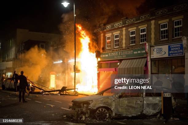 Shop and police car burn as riot police try to contain a large group of people on a main road in Tottenham, north London on August 6, 2011. Two...