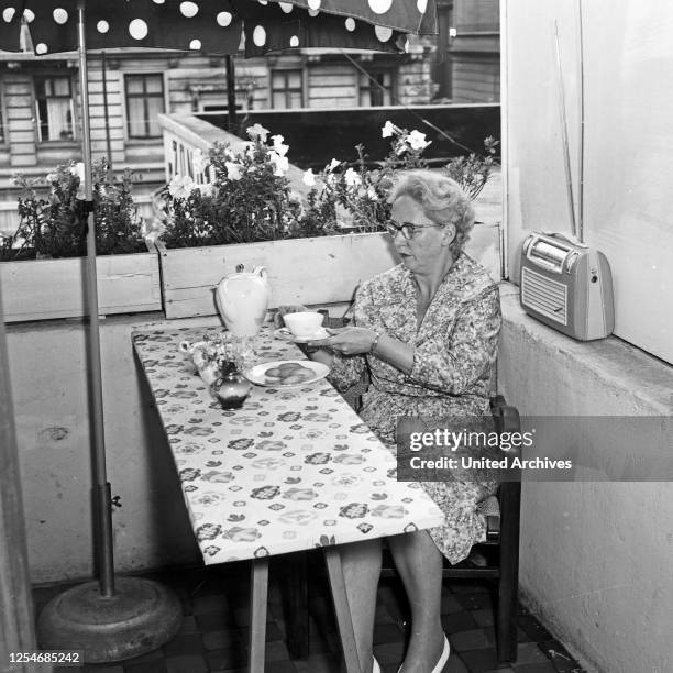 Eine Frau sitzt auf ihrem Balkon und trinkt Kaffee, Deutschland 1950er Jahre.