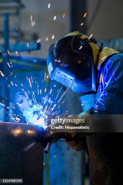 soldador irreconocible que trabaja en una fábrica con ropa de trabajo protectora - soldar fotografías e imágenes de stock