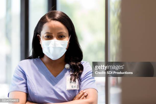 fröhliche krankenschwester trägt schutzmaske während coronavirus-epidemie - essenzielle berufe und dienstleistungen stock-fotos und bilder