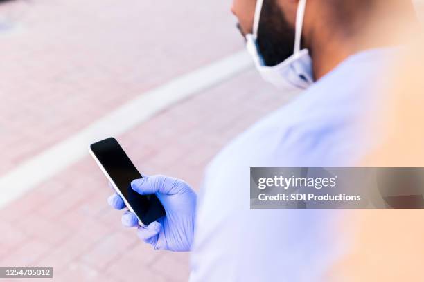 doctor scrolls on phone screen while wearing protective gloves - surgical glove stock pictures, royalty-free photos & images
