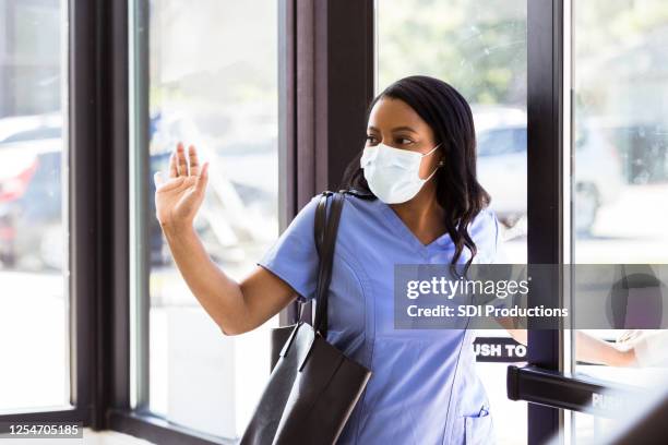 nurse wearing protective mask waves as she leaves work - nurse leaving stock pictures, royalty-free photos & images