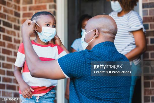 father helps son put on protective face mask - covid 19 stock pictures, royalty-free photos & images