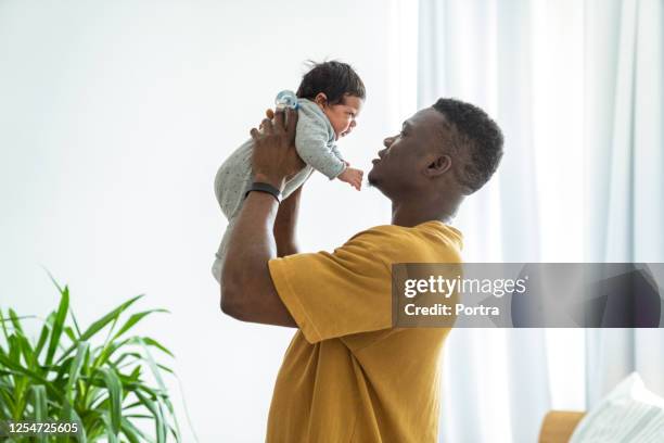 verspielter vater heben neugeborenes - black man holding baby stock-fotos und bilder