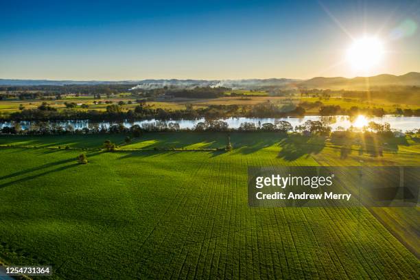 farming land with green fields, river and mountain range at sunset - farm australia stock pictures, royalty-free photos & images