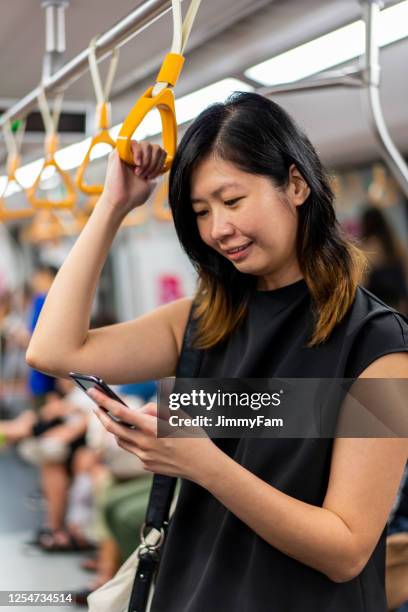 asian female millennial using smart mobile phone inside mrt - singapore mrt stock pictures, royalty-free photos & images