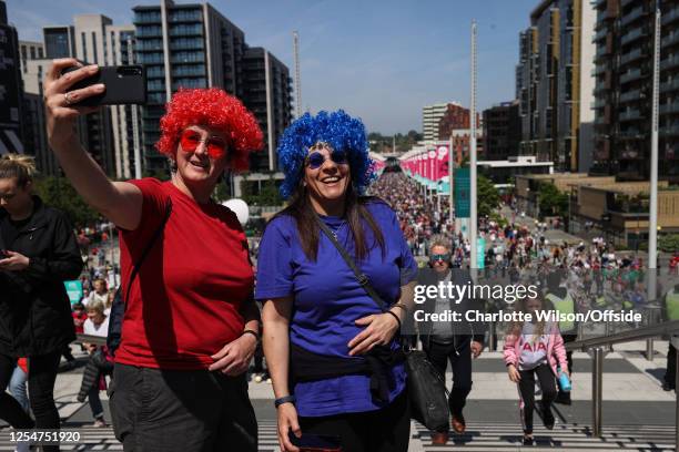 Fans in red and blue afro wigs take a selfie with Wembley Way behind them ahead of the Vitality Women's FA Cup Final between Chelsea and Manchester...