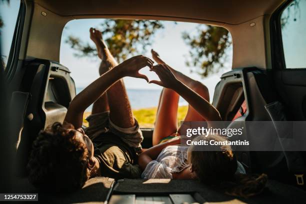 het houden van jong paar dat van overzeese mening van open autoboomstam geniet - couple on the beach with car stockfoto's en -beelden