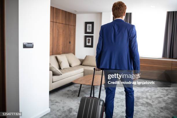 empresario entrando en la suite del hotel y tirando de la maleta - red head man fotografías e imágenes de stock