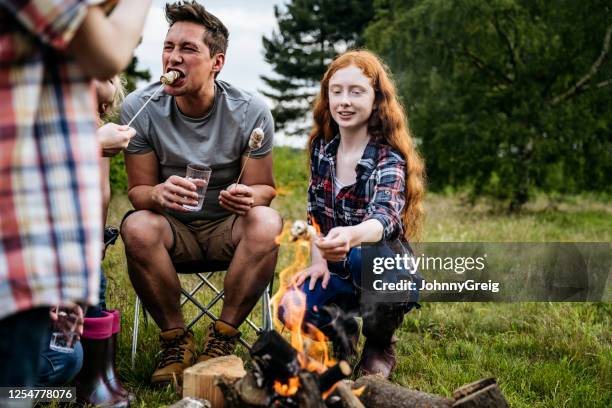 father eating marshmallows with children on camping trip - camping campfire stock pictures, royalty-free photos & images